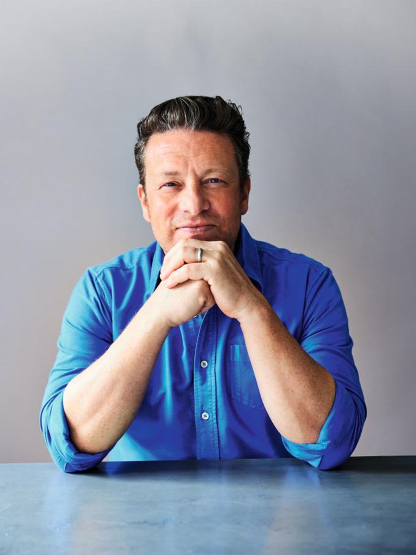 Jamie Oliver in einem blauen Hemd vor einer grauen Wand