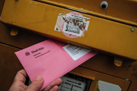 Jemand wirft einen pinken Wahlumschlag in einen Briefkasten