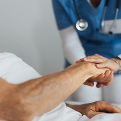 Eine Pflegerin hält die Hand eines älteren Patientin