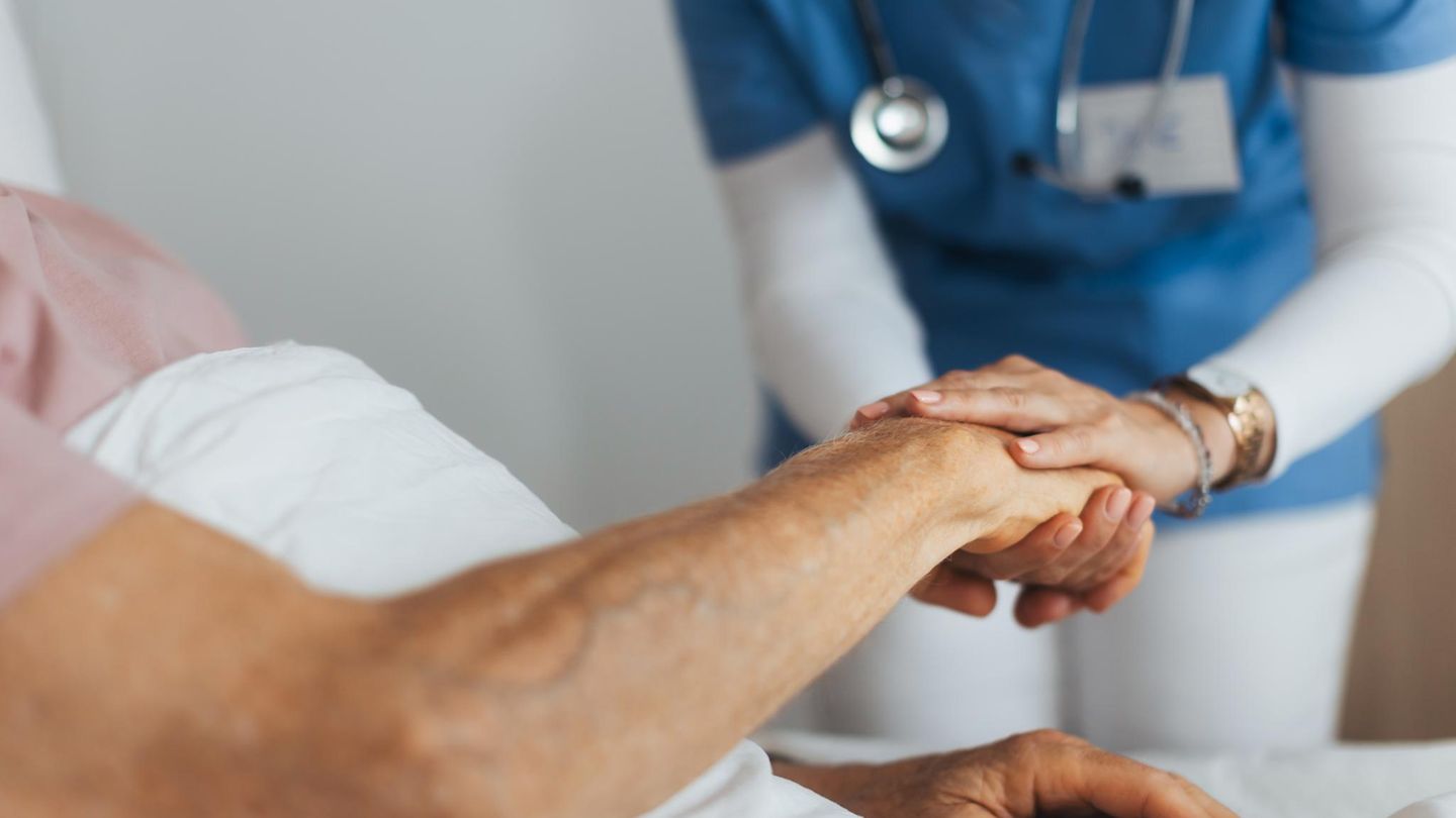 Pflege Eine Pflegerin hält die Hand eines älteren Patientin