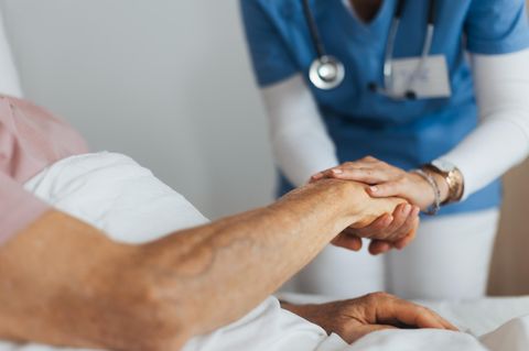 Eine Pflegerin hält die Hand eines älteren Patientin