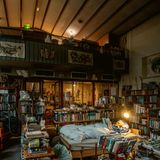 Ein Mann liest im Bett inmitten einer Bücherlandschaft.