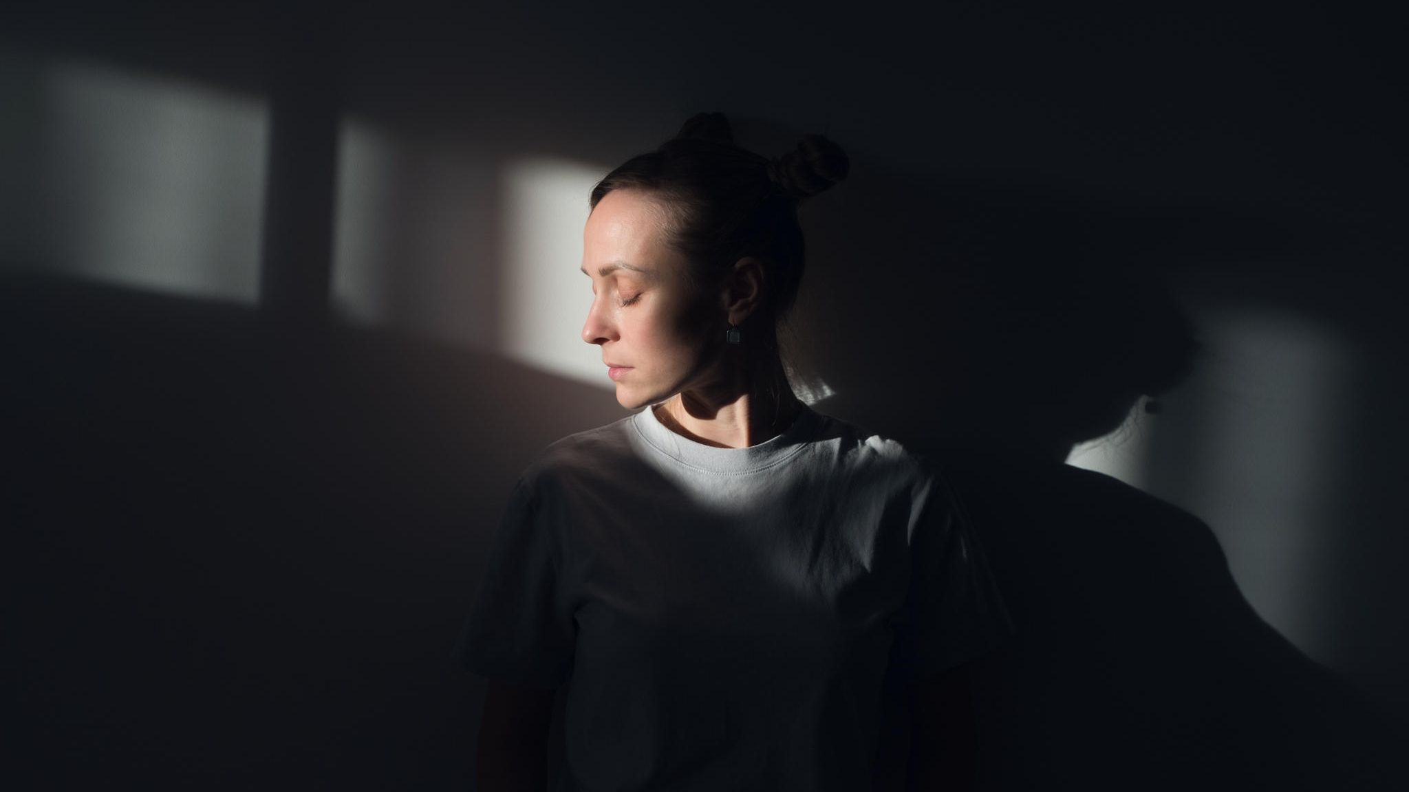 Frau steht im Lichtkegel eines dunklen Zimmers