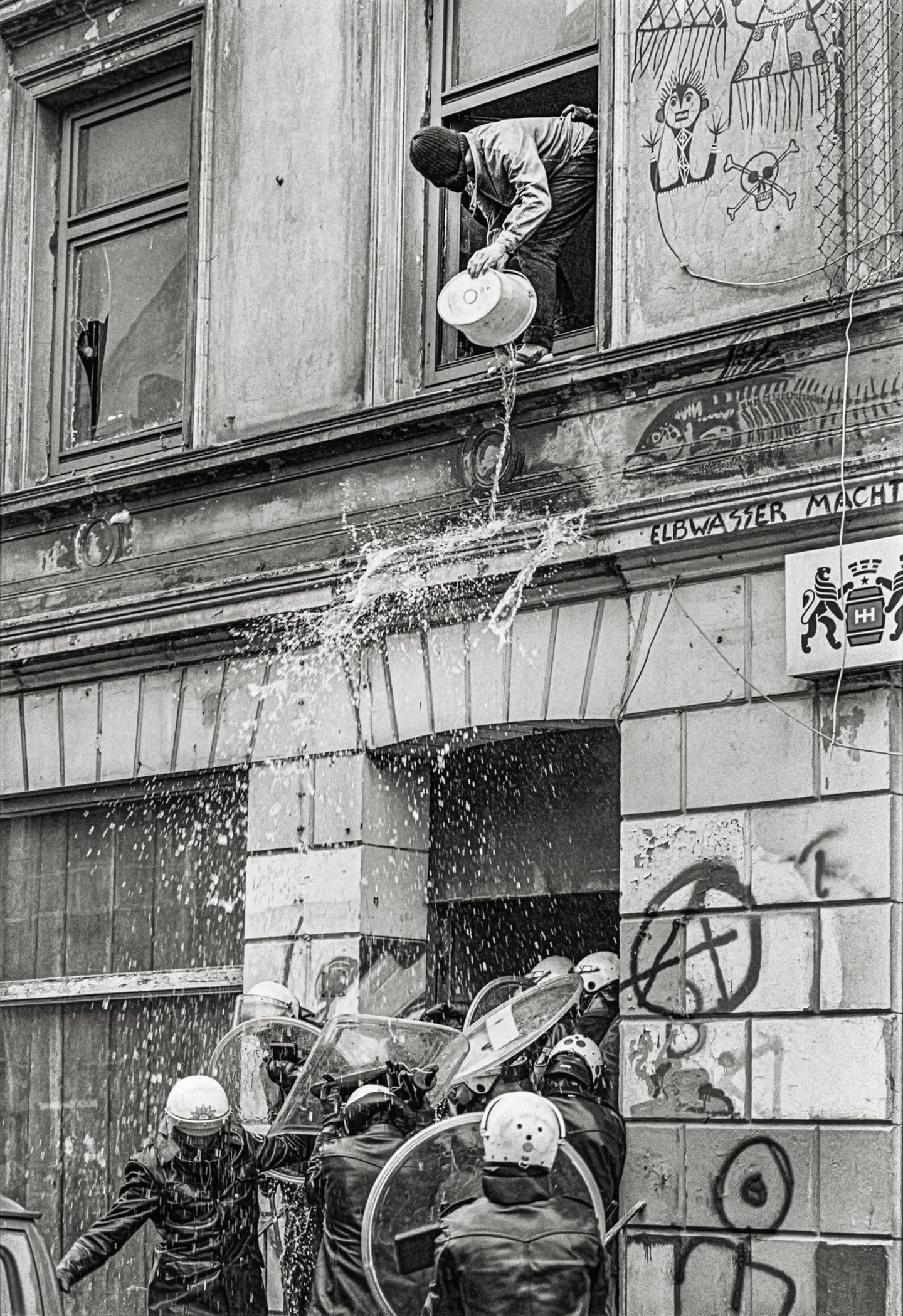 Ein Hausbesetzer schüttet einen Eimer Wasser auf Polizisten