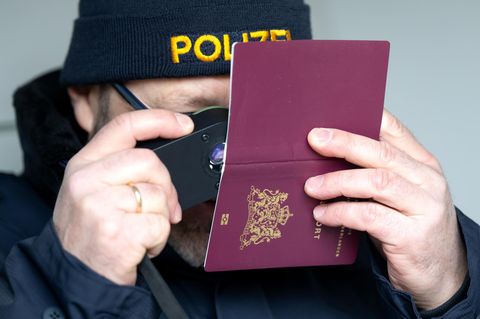 Ein Polizist untersucht einen Reisepass (Symbolbild Migration)