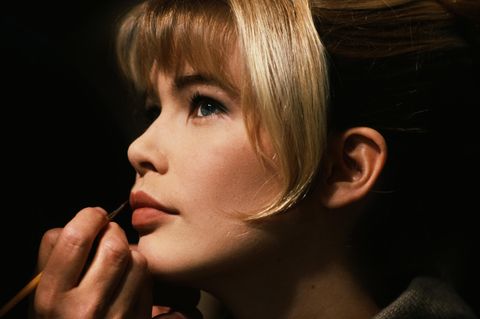 Mit einem Pinsel trägt eine Hand Farbe auf Claudia Schiffers Lippen auf