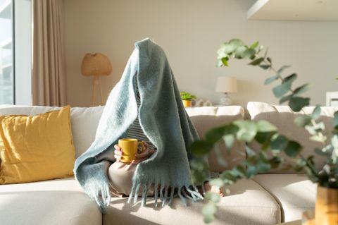 In Decke eingehüllte Frau sitz auf dem Sofa