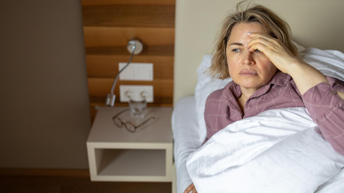 Erschöpfte Frau fasst sich im Bett liegend an den Kopf