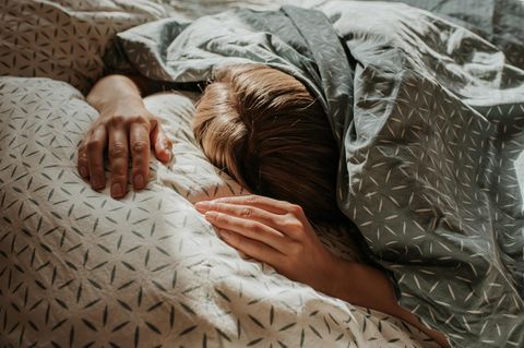 Eine Frau liegt im Bett unter ihrer Decke