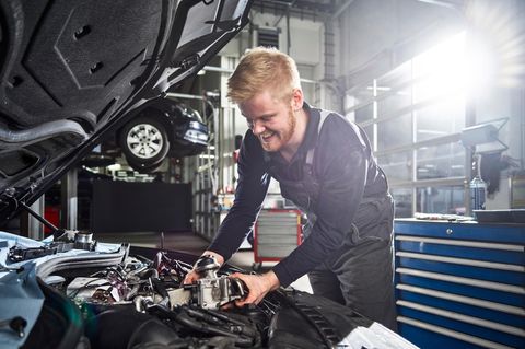 Kfz-Mechatroniker arbeitet am Motor eines Autos in der Werkstatt