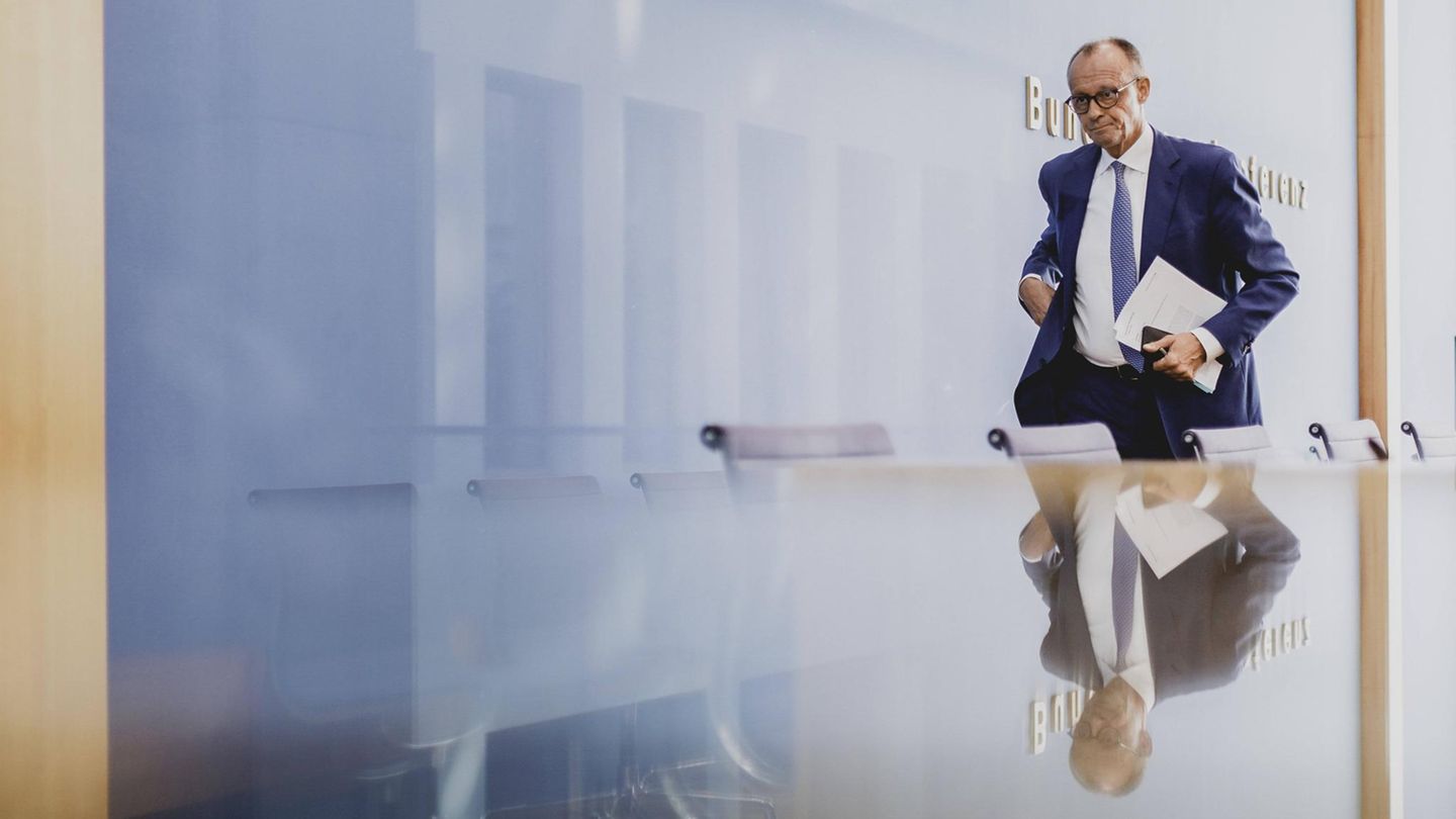 Ein Mann im Anzug (Friedrich Merz) geht eine Stuhlreihe entlang, vor der er sich spiegelt.