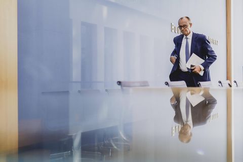 Ein Mann im Anzug (Friedrich Merz) geht eine Stuhlreihe entlang, vor der er sich spiegelt.