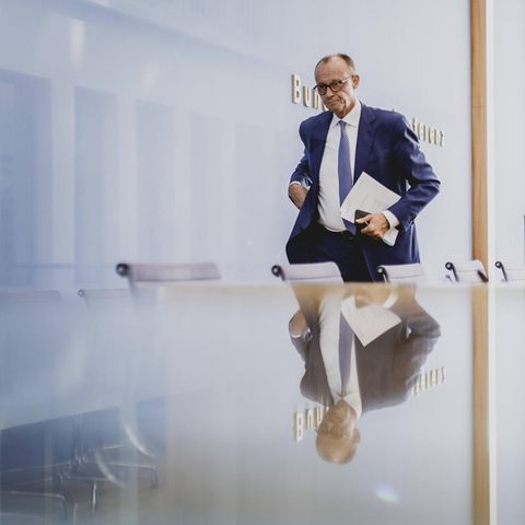 Ein Mann im Anzug (Friedrich Merz) geht eine Stuhlreihe entlang, vor der er sich spiegelt.