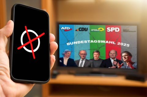 Bundestagswahl 2025 live im TV: Eine Hand hält ein Handy mit Wahlkreuz, im Hintergrund TV Bildschirm mit den Kandidaten