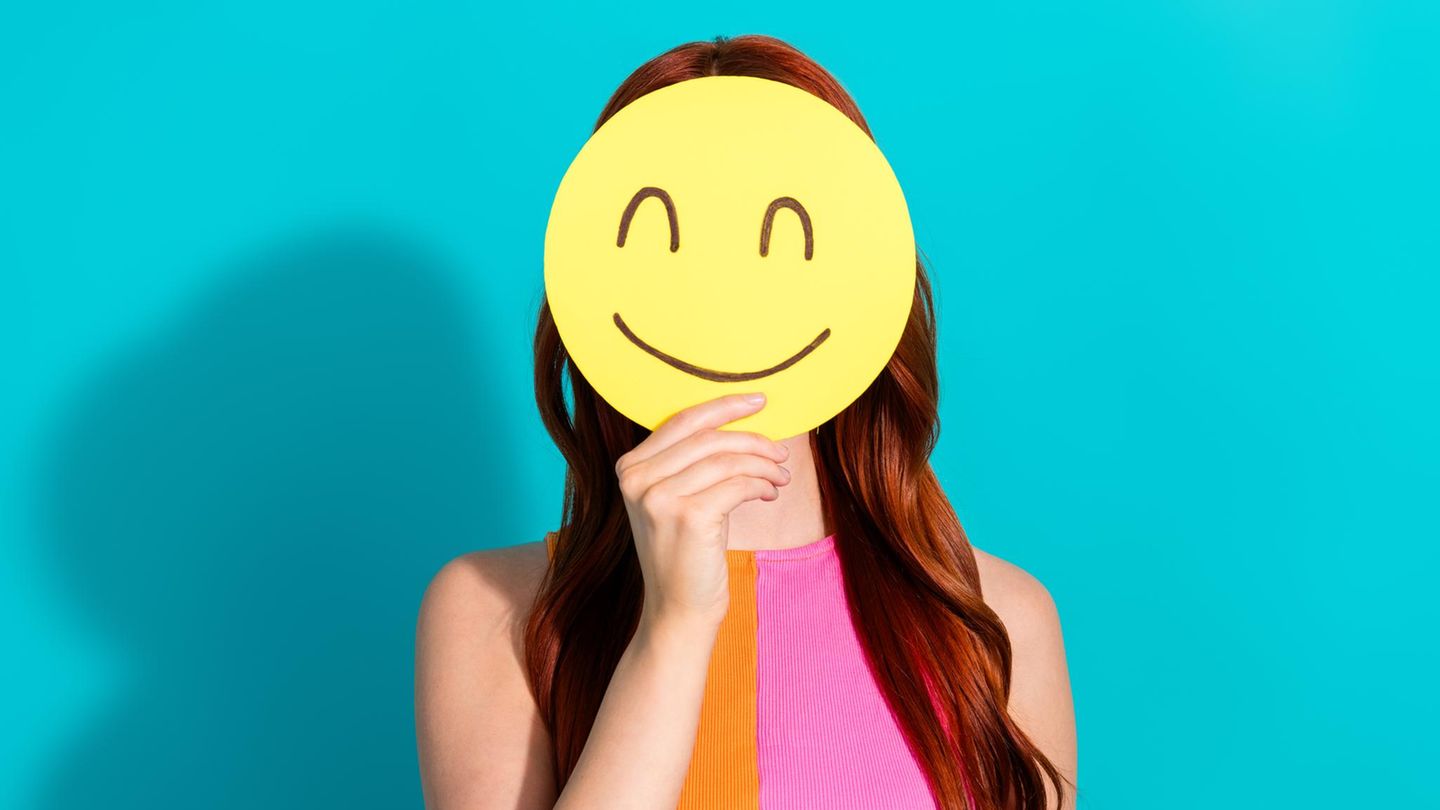 Bebilderung zum Thema "Freundlichkeit": Eine Frau mit einem lächelnden Smiley vor dem Gesicht Bebilderung zum Thema "Freundlichkeit": Eine Frau mit einem lächelnden Smiley vor dem Gesicht