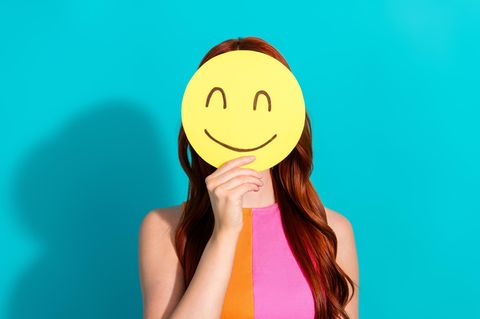 Bebilderung zum Thema "Freundlichkeit": Eine Frau mit einem lächelnden Smiley vor dem Gesicht