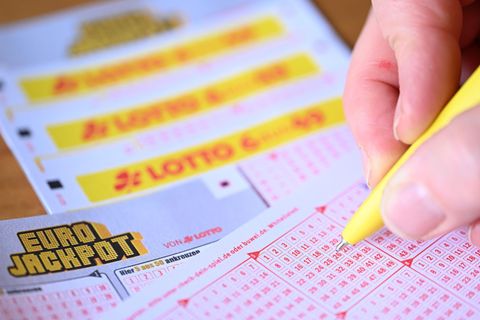 Eine rechte Hand kreuzt mit gelbem Kuli Zahlen auf einem Eurojackpot-Lotto-Schein an