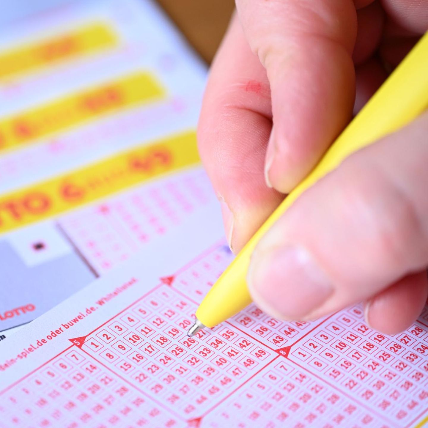 Eine rechte Hand kreuzt mit gelbem Kuli Zahlen auf einem Eurojackpot-Lotto-Schein an