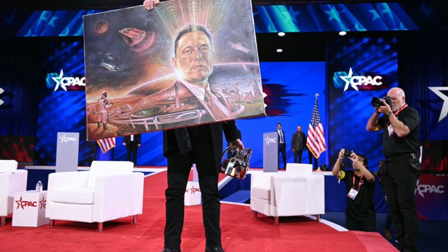 Elon Musk hält ein Bild von sich hoch