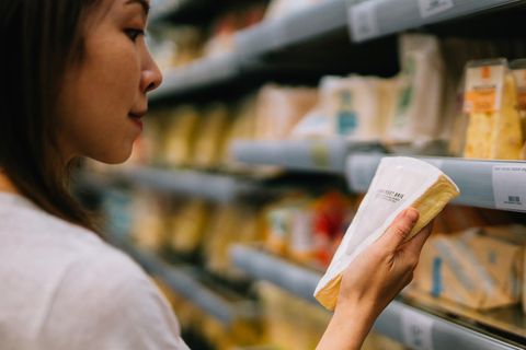Eine Frau im Supermarkt betrachtet die Produktinformationen eines Stückes Käse