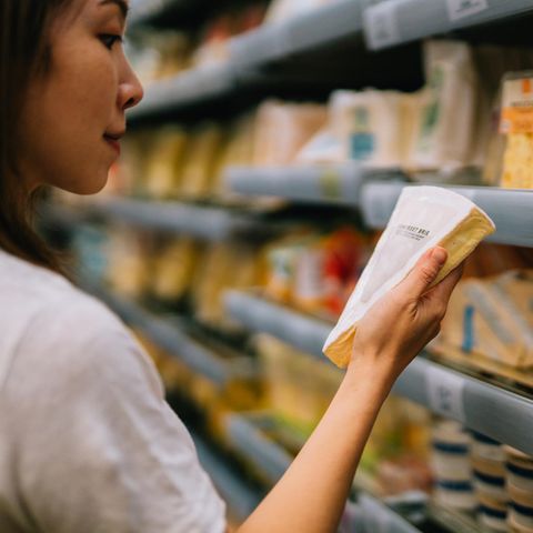 Eine Frau im Supermarkt betrachtet die Produktinformationen eines Stückes Käse