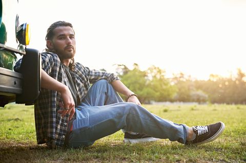 Ein Mann sitzt mit seinen Vans an sein Auto gelehnt