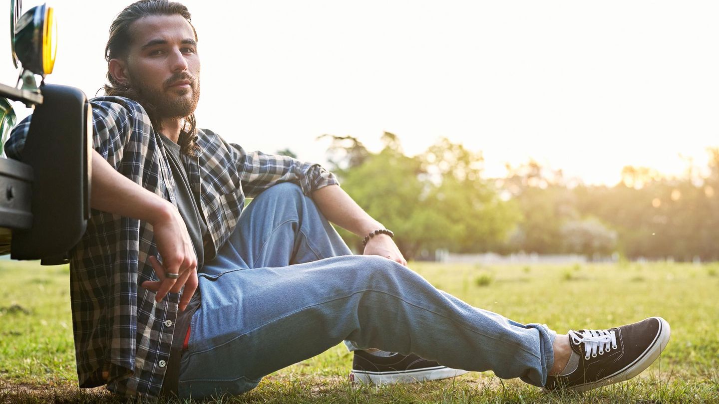 Ein Mann sitzt mit seinen Vans an sein Auto gelehnt