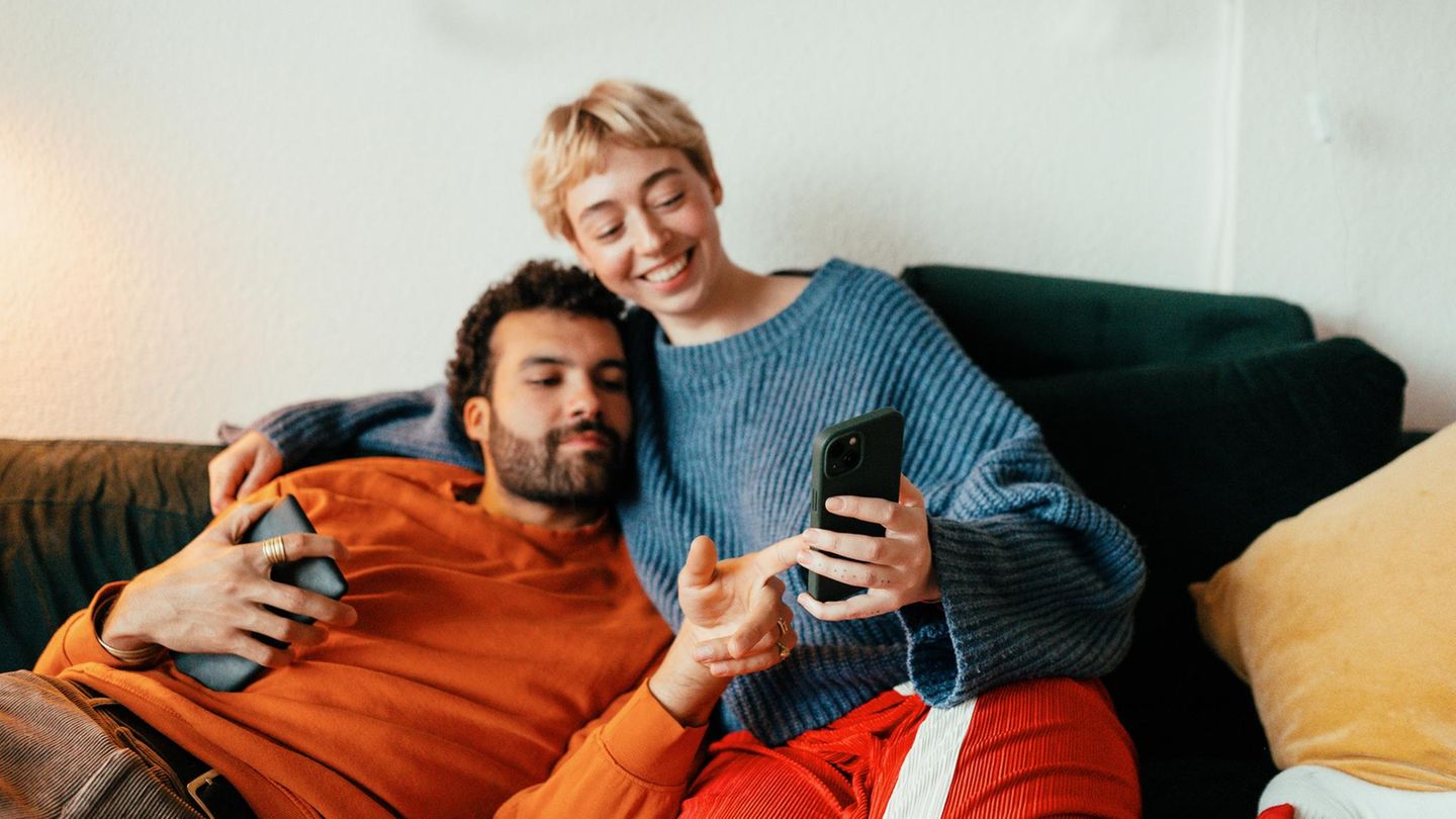Handy in der Hand, ein Paar sitzt auf dem Sofa und schaut ins Handy