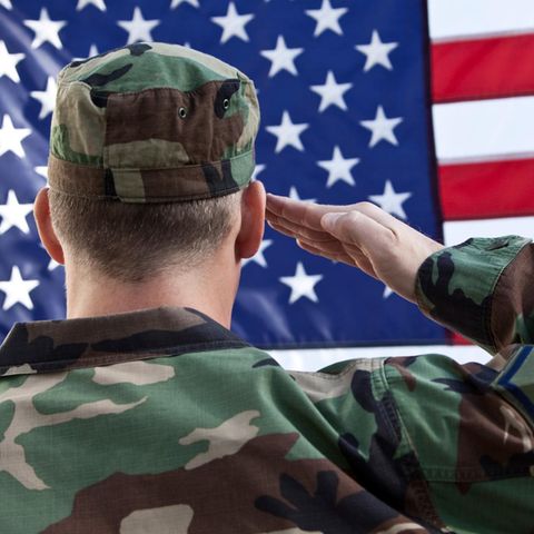 Ein Soldat in Tarn-Uniform salutiert vor einer Flagge der USA