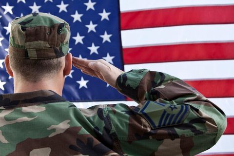 Ein Soldat in Tarn-Uniform salutiert vor einer Flagge der USA