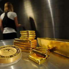 Goldbarren und Münzen liegen in einem Tresorraum, eine Frau schließt sie ein