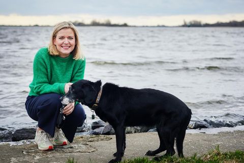 Die Autorin kniet neben ihrer Hündin Lyra am Ufer der Elbe.