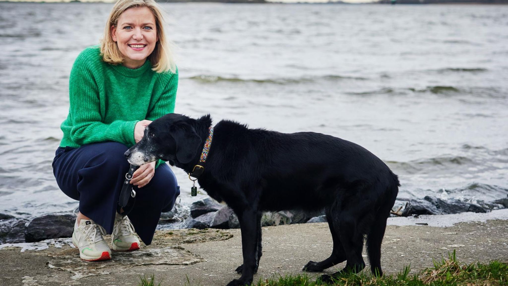 Die Autorin kniet neben ihrem Hund Lyra am Ufer der Elbe