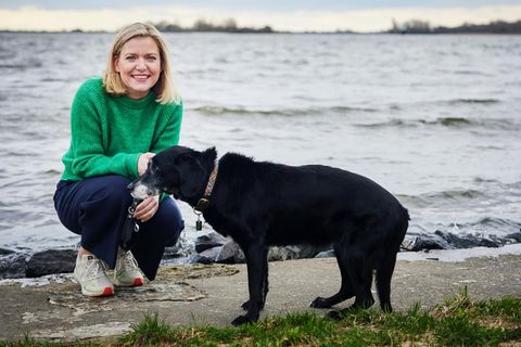 Die Autorin kniet neben ihrem Hund Lyra am Ufer der Elbe