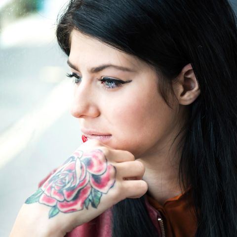 Eine Frau mit Rosen-Tattoo auf dem rechten Handrücken schaut aus einem Fenster