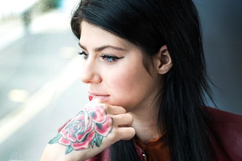 Eine Frau mit Rosen-Tattoo auf dem rechten Handrücken schaut aus einem Fenster