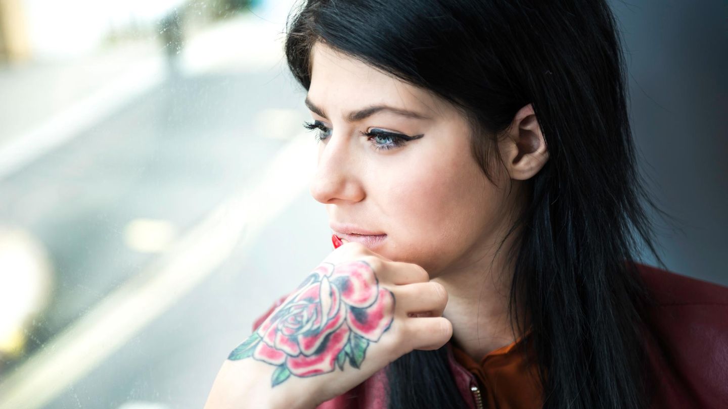Eine Frau mit Rosen-Tattoo auf dem rechten Handrücken schaut aus einem Fenster