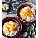    Zutaten für 4 Personen:   200 g weißer Klebreis  300 ml Kokosmilch  5-6 EL Zucker  1 große aromatische, reife Mango (oder 2 kleine)  4 TL ungeschälte Sesamsaat  Salz     Zubereitung  1. Den Klebreis mindestens drei Stunden oder besser noch länger, zum Beispiel über Nacht, in reichlich kaltem Wasser einweichen.      2. Den Reis in ein Sieb abgießen, abtropfen lassen, in einen Topf geben, mit Wasser bedecken und in kreisenden Bewegungen waschen. Dabei gibt der Reis Stärke ab, das Wasser wird trüb und milchig. Abgießen und erneut, eventuell auch mehrmals, waschen, bis das Wasser so gut wie klar ist.      3. Den abgegossenen Reis mit 500 Milliliter Wasser und einer Prise Salz in den Topf geben, aufkochen, dann die Hitze reduzieren und auf niedriger Stufe zehn bis 15 Minuten köcheln lassen, bis das Wasser aufgesogen ist. Den Topf vom Herd nehmen.      4. Inzwischen die Kokosmilch gut verrühren. 200 Milliliter Kokosmilch in einem kleinen Topf erhitzen, eine Prise Salz und drei Esslöffel Zucker unterrühren. Die heiße Kokosmilch über den gegarten Reis gießen, den Topf abdecken und etwa 15 Minuten ziehen lassen, dabei zwischendurch einmal umrühren.      5. Währenddessen die Mango(s) schälen, das Fruchtfleisch vom Stein lösen und die Hälfte davon in Spalten schneiden. Das übrige Fruchtfleisch in einen Mixbecher geben und mit dem Stabmixer pürieren.      6. Den Sesam in einer Pfanne ohne Fett kurz anrösten. Die übrige Kokosmilch in einem kleinen Topf erhitzen und mit dem restlichen Zucker süßen.      7. Den warmen Kokosreis auf Schalen verteilen und mit der süßen Kokosmilch begießen. Die Mangospalten darauf anrichten, dann das Mangopüree darüber geben und mit dem gerösteten Sesam bestreuen.