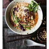    Zutaten für 4 Personen:  Für das Tofuhack  20 g Ingwer  2 Knoblauchzehen  250 g Tofu Natur  1 EL Pflanzenöl  1 EL geröstetes Sesamöl  2 EL Tomatenmark  4 EL dunkle Sojasauce     Für die Brühe  ca. 800 ml gute, kräftige Gemüsebrühe  500 ml Sojamilch  30-40 g helles, mildes Miso  100 g Tahin (Sesammus)  3-4 EL dunkle Sojasauce  2-3 TL Limettensaft  schwarzer Pfeffer aus der Mühle  Salz     Für Bohnen und Nudeln  300 g grüne Bohnen  200 g Ramennudeln  2-3 EL Cashewkerne Natur  1 EL Sriracha-Sauce  1 EL Pflanzenöl  2 EL Korianderblätter  1 EL rote Shiso (asiatische Kresse)  Salz     Zubereitung  1. Für das Tofuhack Ingwer und Knoblauchzehen schälen und fein hacken. Den Tofu gut trocken tupfen, dann fein zerkrümeln. Pflanzenöl und Sesamöl in einer beschichteten Pfanne erhitzen und die Tofukrümel darin zwei bis drei Minuten kräftig anbraten. Ingwer und Knoblauch dazugeben und kurz mit anbraten. Tomatenmark und Sojasauce unterrühren, abschmecken und die Pfanne beiseitestellen.      2. Für die Brühe Gemüsebrühe, Sojamilch, Miso, Tahin und drei Esslöffel Sojasauce in einen Topf geben und bei mittlerer Hitze etwa fünf Minuten offen einkochen lassen, dann mit restlicher Sojasauce, Limettensaft, etwas Salz und Pfeffer abschmecken und vom Herd nehmen. Falls die Brühe krisselig wird (gerinnt), mit dem Stabmixer kurz pürieren, dann wird sie wieder glatt und cremig.      3. Inzwischen die Bohnen putzen, waschen, in kochendem Salzwasser sieben bis zehn Minuten blanchieren, dann in ein Sieb abgießen, kalt abbrausen und abtropfen lassen.     4. Währenddessen die Nudeln nach Packungsangaben kochen, in ein Sieb abgießen, kalt abbrausen und abtropfen lassen.      5. Cashewkerne grob hacken, in einer Pfanne ohne Fett kurz anrösten und beiseitestellen. Sriracha-Sauce und Öl verrühren.      6. Die Brühe erhitzen. Das Tofuhack in der Pfanne unter Rühren noch mal heiß werden lassen.      7. Tofuhack, Nudeln und Bohnen in Schalen geben, mit der sehr heißen Brühe begießen, das Sriracha-Öl hineinträufeln und mit Cashews, Koriander und Shiso bestreuen. 