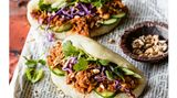   Zutaten für 4 Personen (ergibt 8 Stück):  Für die Buns  300 g Weizenmehl (Type 405) plus etwas zum Bemehlen  ½ Pck. Trockenhefe  1 TL Zucker  1 knapper TL Salz  2 EL Pflanzenöl plus etwas zum Bestreichen     Für die Jackfruit-Füllung  1 Zwiebel  1-2 Knoblauchzehen  15 g Ingwer  1 rote Chili  225 g Jackfruit in Wasser aus der Dose (Abtropfgewicht)  2 EL Pflanzenöl  3 EL Tomatenmark  3 EL dunkle Sojasauce  1 EL Zucker (oder Agavensirup)  1-2 EL Limettensaft     Für die Rohkost-Füllung  1 Frühlingszwiebel  100 g Rotkohl  1 Minigurke  3 EL geröstete, gesalzene Erdnusskerne  2 EL Korianderblätter     Zubereitung:  1. Für die Buns Mehl, Hefe, Zucker und Salz in einer Schüssel mischen. 170 Milliliter handwarmes Wasser und das Öl dazugeben und von Hand etwa fünf Minuten gründlich zu einem glatten, elastischen Teig verkneten. Die Schüssel abdecken und den Teig an einem warmen Ort etwa 60 Minuten gehen lassen, bis er das doppelte Volumen erreicht hat.      2. Backpapier in acht etwa zwölf × zwölf Zentimeter große Quadrate schneiden. Den Teig auf die leicht bemehlte Arbeitsfläche geben, in acht gleich große Portionen (à etwa 60 Gramm) teilen und zu Kugeln formen. Mit dem Nudelholz zu etwa zehn Zentimeter großen Teigkreisen ausrollen und mit etwas Öl bestreichen. Je einen Teigfladen auf ein Backpapierquadrat legen und den Fladen mittig locker falten, sodass ein Halbkreis entsteht. Abdecken und 30 bis 45 Minuten gehen lassen.     3. Inzwischen für die Jackfruit-Füllung Zwiebel, Knoblauchzehe(n) und Ingwer schälen und fein hacken. Die Chili waschen, entkernen und fein hacken. Jackfruit in ein Sieb geben, kalt abbrausen und kleiner zupfen. Das Öl in einer tiefen Pfanne erhitzen. Zwiebeln, Knoblauch, Ingwer und Chili darin kurz anbraten. Dann Jackfruit, 200 Milliliter Wasser, Tomatenmark, Sojasauce, Zucker und Limettensaft dazugeben, aufkochen und bei kleiner Hitze und unter gelegentlichem Rühren etwa zehn Minuten dicklich einkochen. Vom Herd nehmen.      4. Währenddessen Wasser in einem weiten Topf aufkochen, die Backpapier-Teigpäckchen nebeneinander so in einen großen Dämpfeinsatz legen, dass das Papier den Teig umhüllt (eventuell in zwei Portionen, je nach Größe des Dämpfeinsatzes). Den Deckel auflegen und die Teigstücke zehn Minuten dämpfen. Den Topf vom Herd nehmen und die Buns abgedeckt noch fünf Minuten ruhen lassen (das verhindert, dass sich der Teig durch den Temperaturschock zusammenzieht). Dann erst den Topfdeckel abnehmen, den Dämpfeinsatz herausheben und die Buns lauwarm abkühlen lassen.      5. In der Zwischenzeit für die Rohkostfüllung die Frühlingszwiebel putzen, waschen und in feine Röllchen schneiden. Den Rotkohl in feine Streifen hobeln. Die Gurke waschen und in dünne Scheiben schneiden. Die Erdnüsse hacken.      6. Die Bao-Buns mit heißer oder warmer Jackfruit, Frühlingszwiebeln, Rotkohl, Gurken, Erdnüssen und Koriander füllen.     Tipp: Beim Dämpfvorgang darf der Topfdeckel nicht abgenommen werden, sonst könnten die Buns zusammenfallen.