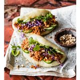    Zutaten für 4 Personen (ergibt 8 Stück):  Für die Buns  300 g Weizenmehl (Type 405) plus etwas zum Bemehlen  ½ Pck. Trockenhefe  1 TL Zucker  1 knapper TL Salz  2 EL Pflanzenöl plus etwas zum Bestreichen     Für die Jackfruit-Füllung  1 Zwiebel  1-2 Knoblauchzehen  15 g Ingwer  1 rote Chili  225 g Jackfruit in Wasser aus der Dose (Abtropfgewicht)  2 EL Pflanzenöl  3 EL Tomatenmark  3 EL dunkle Sojasauce  1 EL Zucker (oder Agavensirup)  1-2 EL Limettensaft     Für die Rohkost-Füllung  1 Frühlingszwiebel  100 g Rotkohl  1 Minigurke  3 EL geröstete, gesalzene Erdnusskerne  2 EL Korianderblätter     Zubereitung:  1. Für die Buns Mehl, Hefe, Zucker und Salz in einer Schüssel mischen. 170 Milliliter handwarmes Wasser und das Öl dazugeben und von Hand etwa fünf Minuten gründlich zu einem glatten, elastischen Teig verkneten. Die Schüssel abdecken und den Teig an einem warmen Ort etwa 60 Minuten gehen lassen, bis er das doppelte Volumen erreicht hat.      2. Backpapier in acht etwa zwölf × zwölf Zentimeter große Quadrate schneiden. Den Teig auf die leicht bemehlte Arbeitsfläche geben, in acht gleich große Portionen (à etwa 60 Gramm) teilen und zu Kugeln formen. Mit dem Nudelholz zu etwa zehn Zentimeter großen Teigkreisen ausrollen und mit etwas Öl bestreichen. Je einen Teigfladen auf ein Backpapierquadrat legen und den Fladen mittig locker falten, sodass ein Halbkreis entsteht. Abdecken und 30 bis 45 Minuten gehen lassen.     3. Inzwischen für die Jackfruit-Füllung Zwiebel, Knoblauchzehe(n) und Ingwer schälen und fein hacken. Die Chili waschen, entkernen und fein hacken. Jackfruit in ein Sieb geben, kalt abbrausen und kleiner zupfen. Das Öl in einer tiefen Pfanne erhitzen. Zwiebeln, Knoblauch, Ingwer und Chili darin kurz anbraten. Dann Jackfruit, 200 Milliliter Wasser, Tomatenmark, Sojasauce, Zucker und Limettensaft dazugeben, aufkochen und bei kleiner Hitze und unter gelegentlichem Rühren etwa zehn Minuten dicklich einkochen. Vom Herd nehmen.      4. Währenddessen Wasser in einem weiten Topf aufkochen, die Backpapier-Teigpäckchen nebeneinander so in einen großen Dämpfeinsatz legen, dass das Papier den Teig umhüllt (eventuell in zwei Portionen, je nach Größe des Dämpfeinsatzes). Den Deckel auflegen und die Teigstücke zehn Minuten dämpfen. Den Topf vom Herd nehmen und die Buns abgedeckt noch fünf Minuten ruhen lassen (das verhindert, dass sich der Teig durch den Temperaturschock zusammenzieht). Dann erst den Topfdeckel abnehmen, den Dämpfeinsatz herausheben und die Buns lauwarm abkühlen lassen.      5. In der Zwischenzeit für die Rohkostfüllung die Frühlingszwiebel putzen, waschen und in feine Röllchen schneiden. Den Rotkohl in feine Streifen hobeln. Die Gurke waschen und in dünne Scheiben schneiden. Die Erdnüsse hacken.      6. Die Bao-Buns mit heißer oder warmer Jackfruit, Frühlingszwiebeln, Rotkohl, Gurken, Erdnüssen und Koriander füllen.     Tipp: Beim Dämpfvorgang darf der Topfdeckel nicht abgenommen werden, sonst könnten die Buns zusammenfallen.