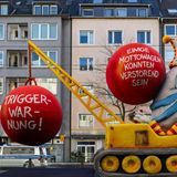 Mottowagen in Düsseldorf: Ein gelber Kran mit einem Clown der eine Triggerwarnung ankündigt