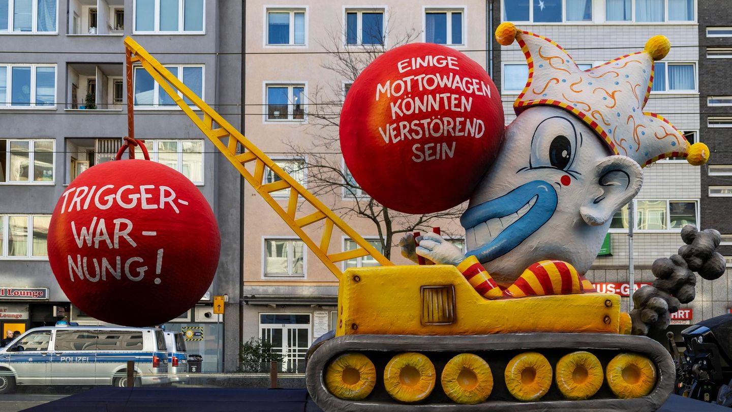 Triggerwarnung in Düsseldorf Mottowagen in Düsseldorf: Ein gelber Kran mit einem Clown der eine Triggerwarnung ankündigt