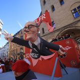 Kölner Rosenmontagszug: Ein Motivwagen mit Friedrich Merz, der durch eine rote Leinwand ragt und das Wort "Scholz" zerreißt