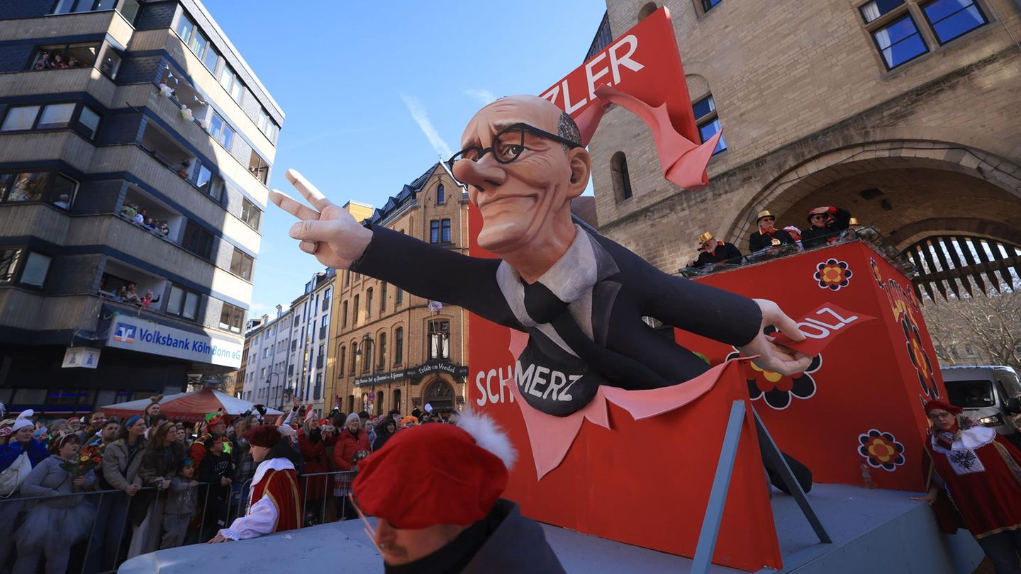 Kölner Rosenmontagszug: Ein Motivwagen mit Friedrich Merz, der durch eine rote Leinwand ragt und das Wort "Scholz" zerreißt