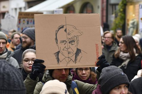 Auf einer Demonstration wird ein Schild mit Friedrich Merz und Donald Trump hochgehalten
