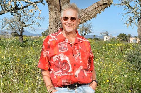 Martin Semmelrogge im roten Hemd auf seiner Finca, im Hintergrund blauer Himmel