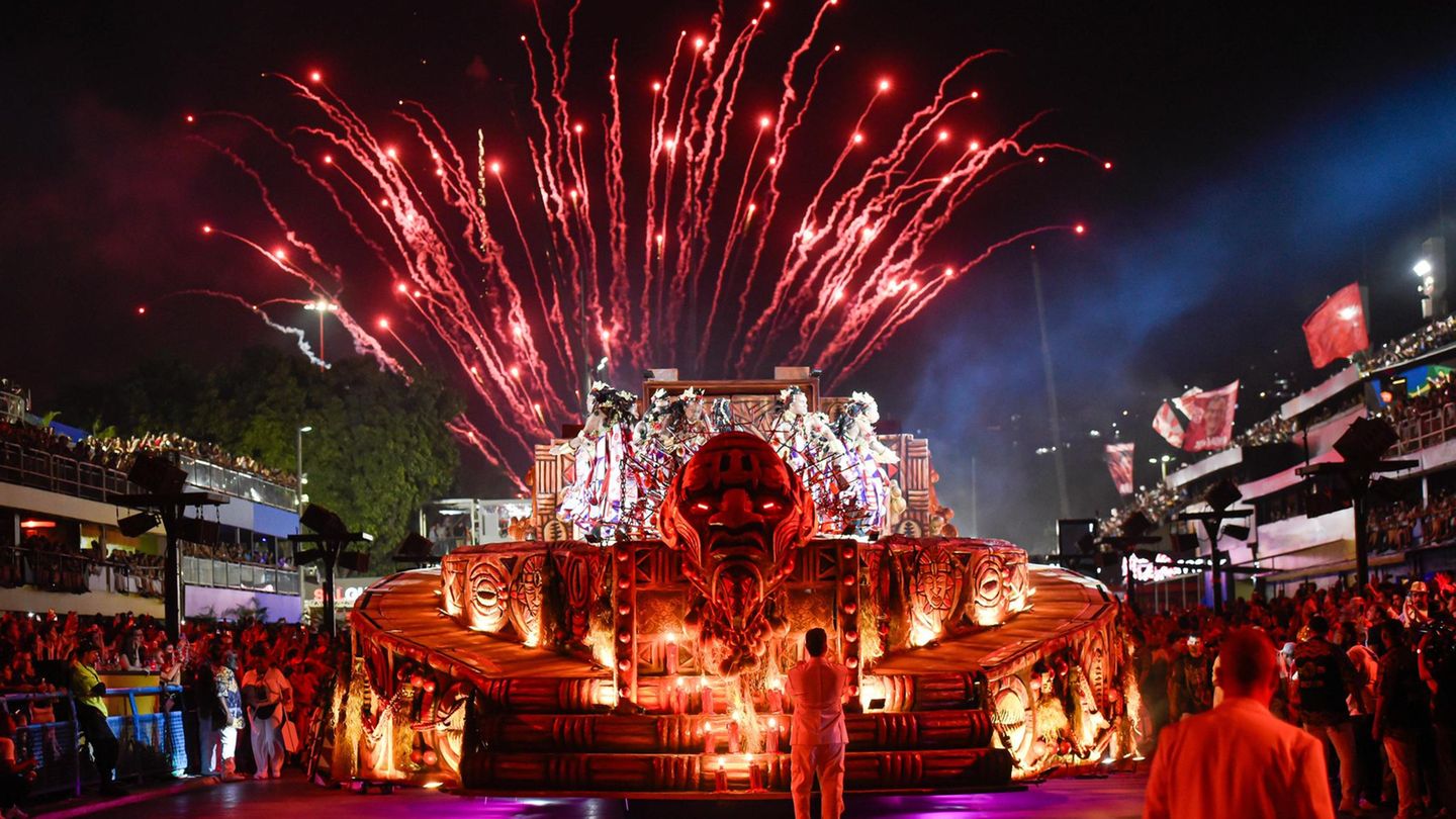 Karneval in Rio de Janeiro: Karnevalswagen zieht über die Straße mit einem roten Feuerwerk im Hintergrund