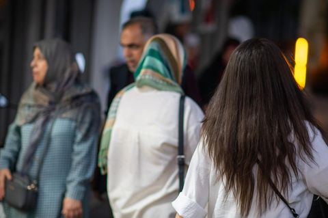 Iran: Eine Frau läuft in Teheran mit offenen Haaren am Abend eine Straße entlang