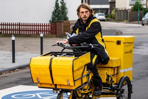 Briefträger fährt die Post auf dem dreirädrigen Lastenfahrrad aus